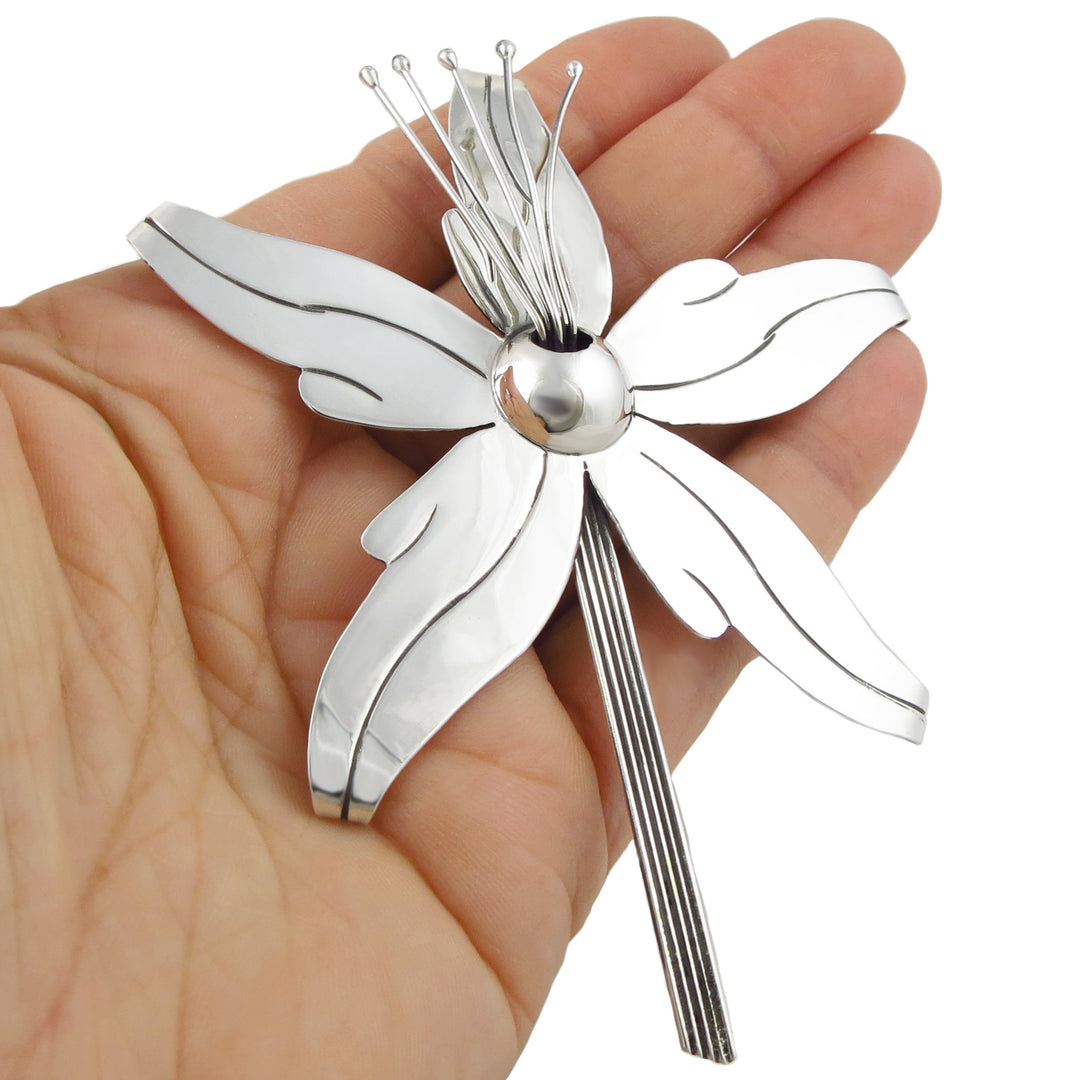 A large orchid pendant in sterling silver held in a person's hand. 