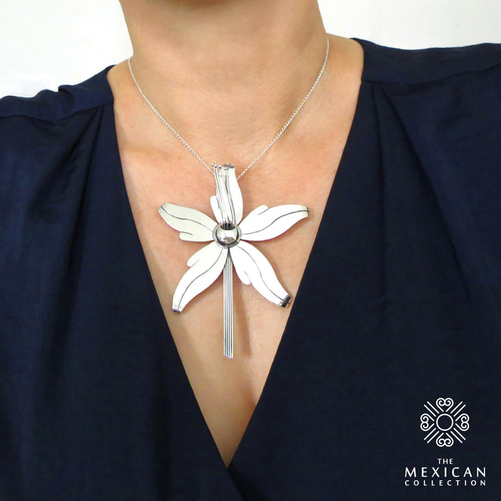 A woman in a blue silk blouse wearing a large silver orchid flower pendant and chain necklace.  