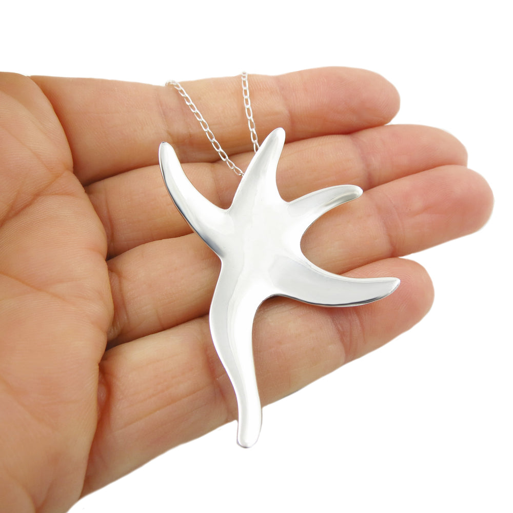 A large UK hallmarked solid 925 sterling silver starfish pendant chain necklace for women held in a hand against a white background