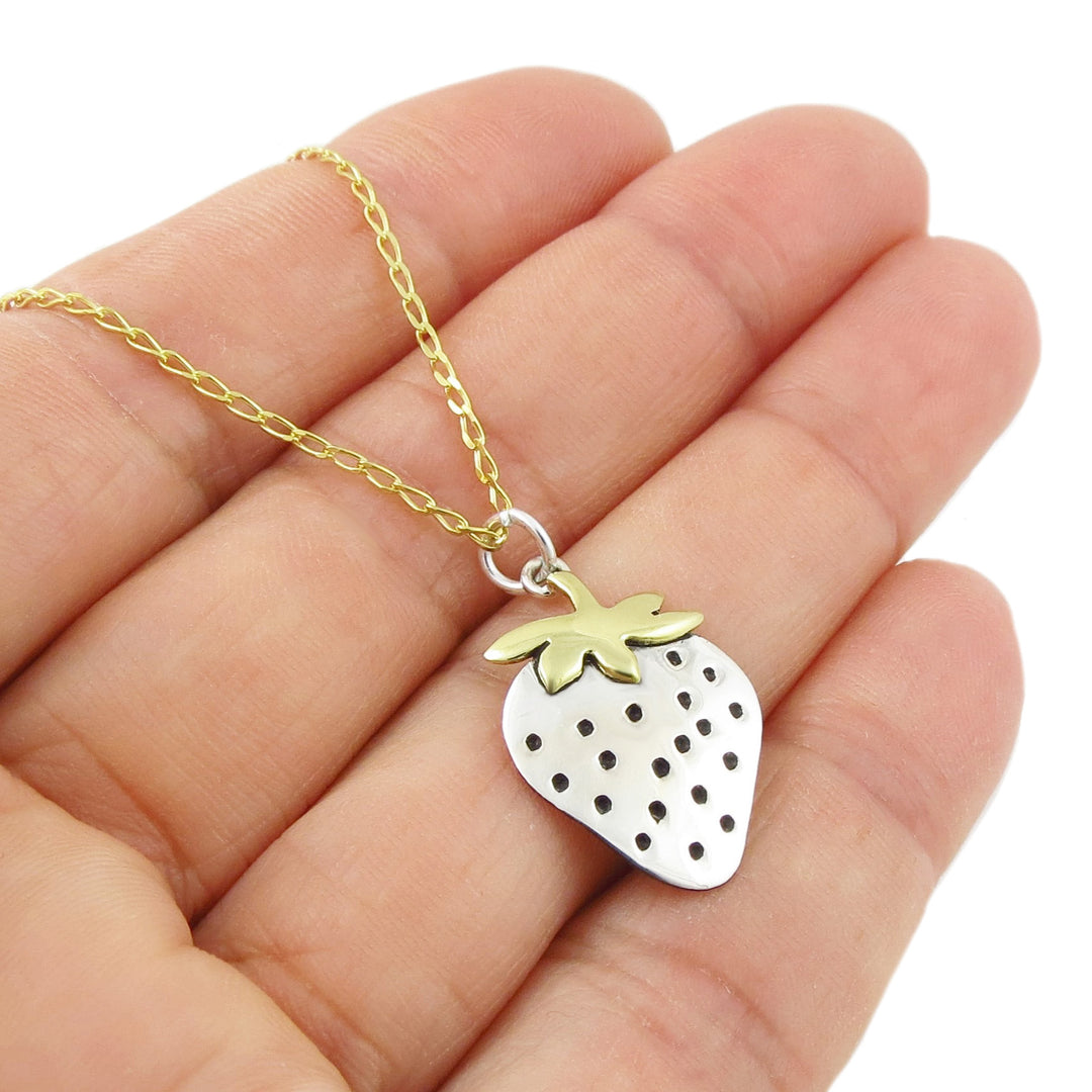 Gold and silver strawberry pendant necklace held in a person's hand. 