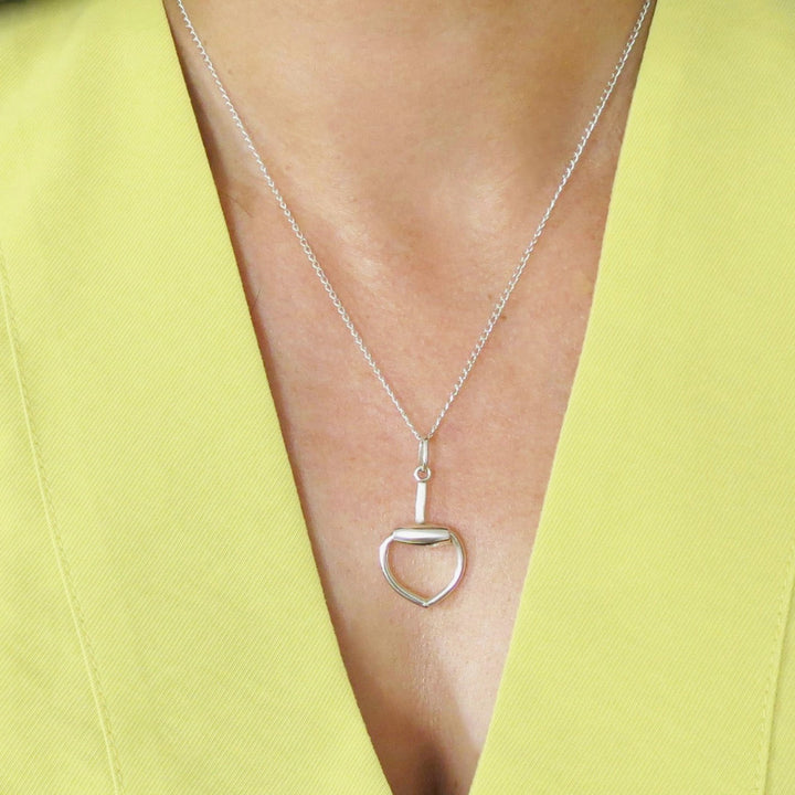 Silver necklace with a heart-shaped horsebit pendant on a chain worn by a person in a yellow outfit.