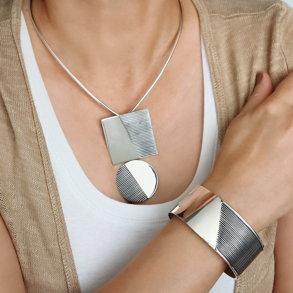 A woman wearing a geometric pattern silver bracelet and matching pendant on a choker