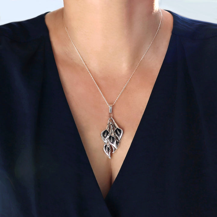 Silver necklace with a calla lily flower pendant on a person wearing a dark blue top.