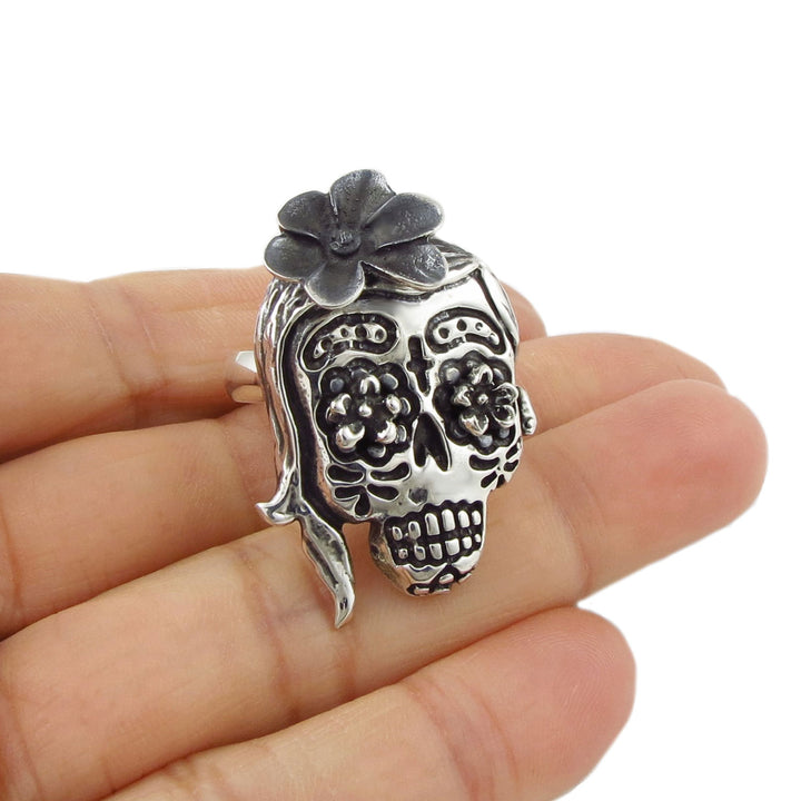 Mexican day of the dead sterling 925 silver skull-shaped ring with floral details held in a hand on a white background
