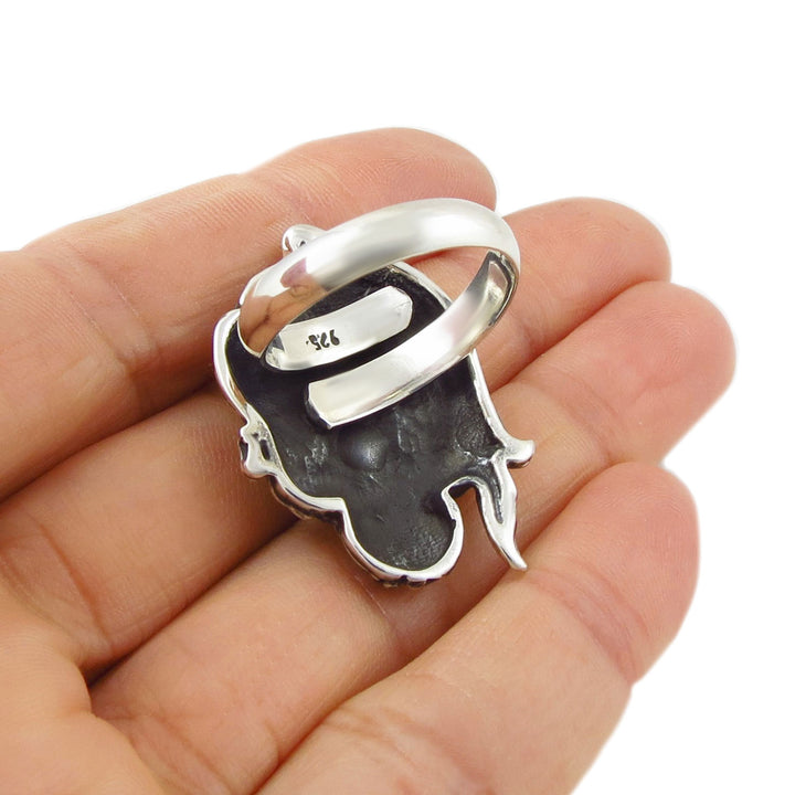 Sterling 925 Silver Mexican sugar skull ring with a spital shank held upside down in a hand against a white background