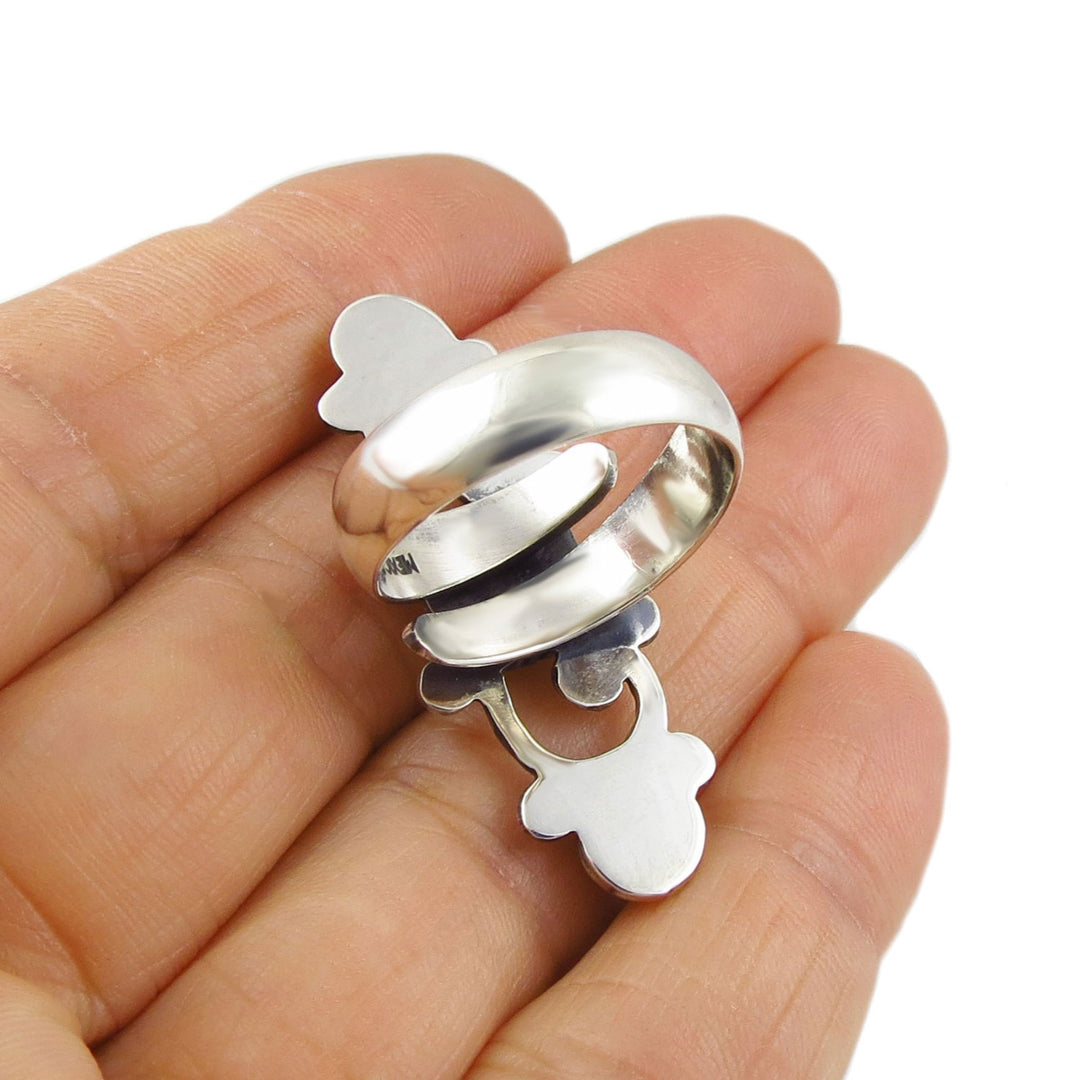 A large sterling 925 silver cocktail ring held upside down to show the adjustable spiral shank held in a hand on a white background