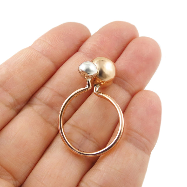 Copper and silver ball bead ring held between fingers on a white background