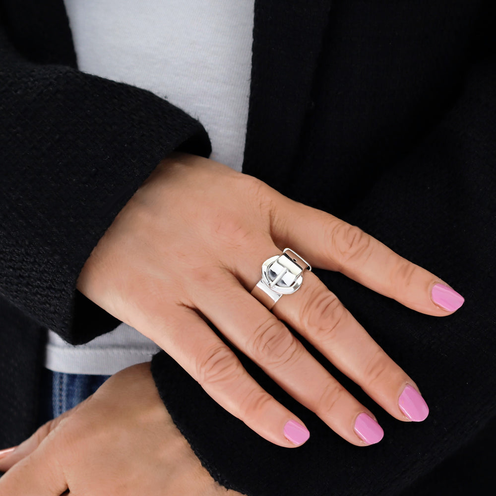 Woman's hand wearing a wide solid 925 sterling silver ring in the shape of a belt and buckle, against a dark background