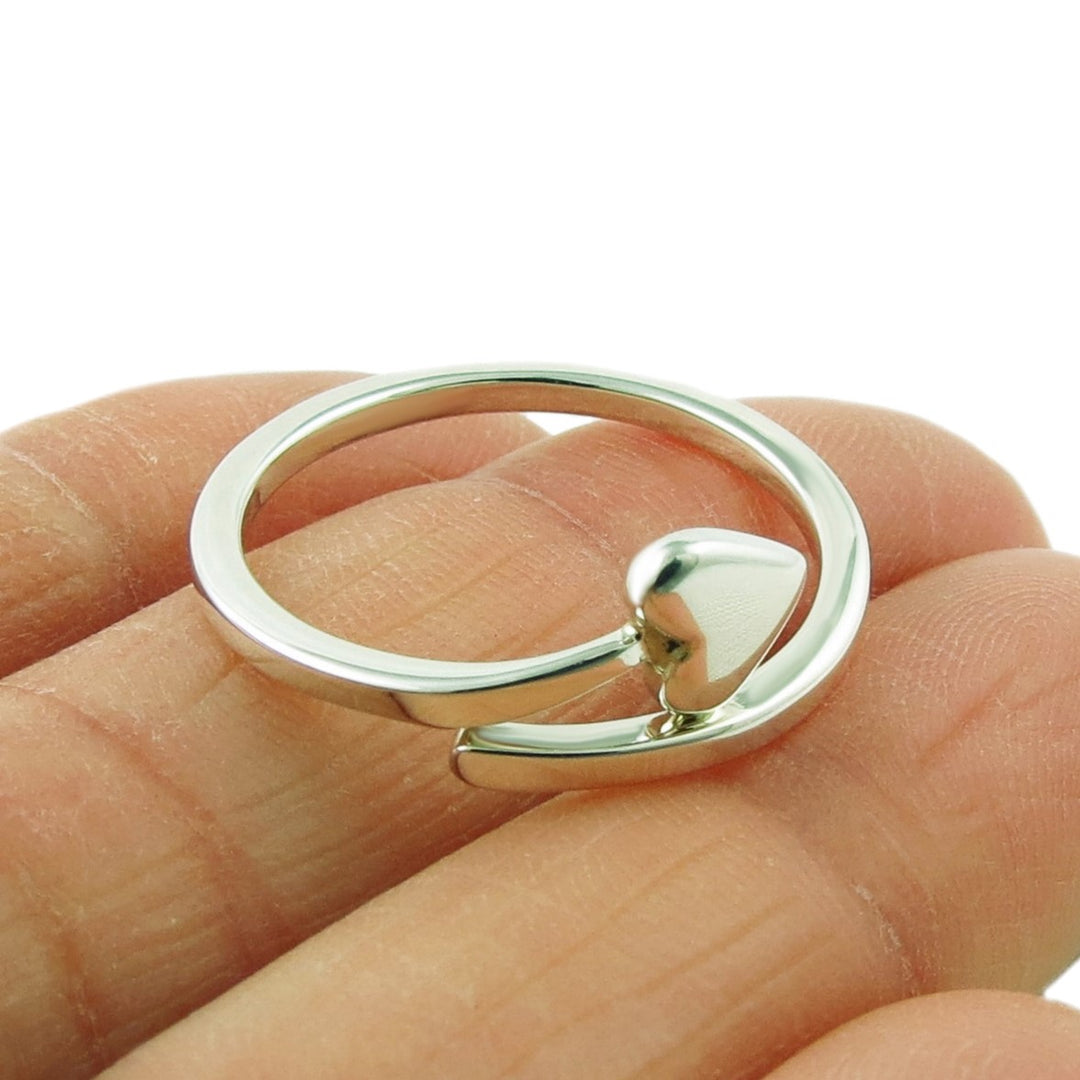 A sterling silver spiral ring with a heart held in a person's fingers. 