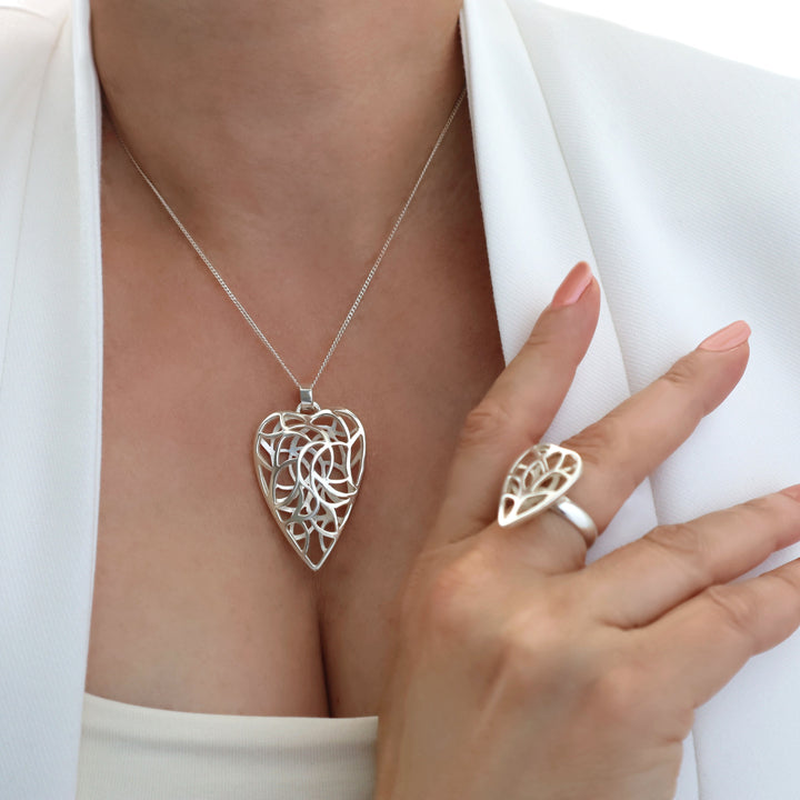 Silver heart-shaped necklace and ring on a person wearing a white blazer.