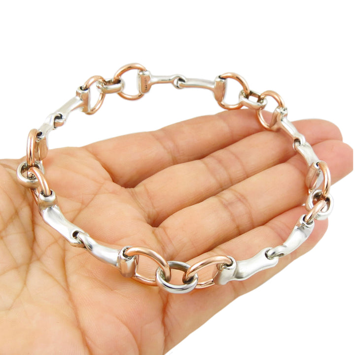Two-tone silver and copper snafflebit equestrian bangle on a hand against a white background