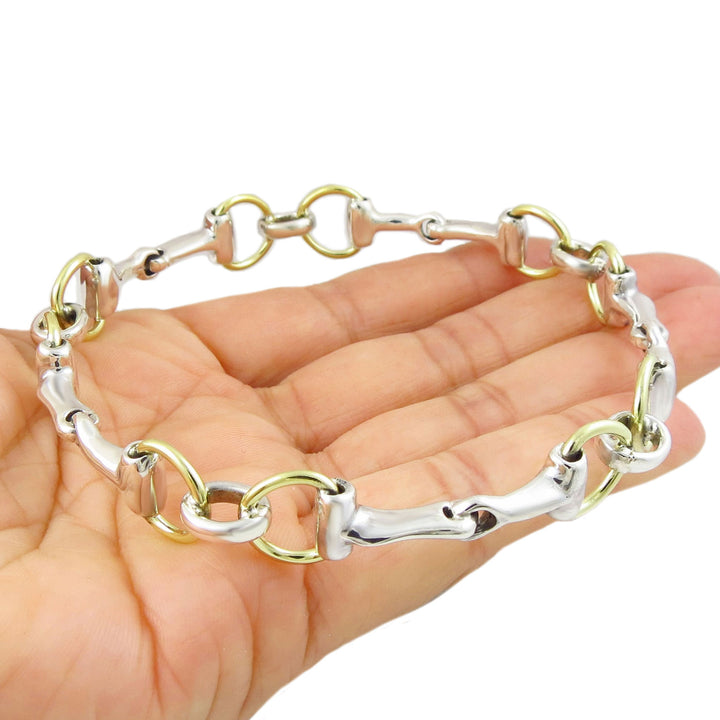 Two-toned gold and sterling silver equestrian snaffelbit bangle bracelet on a hand against a white background