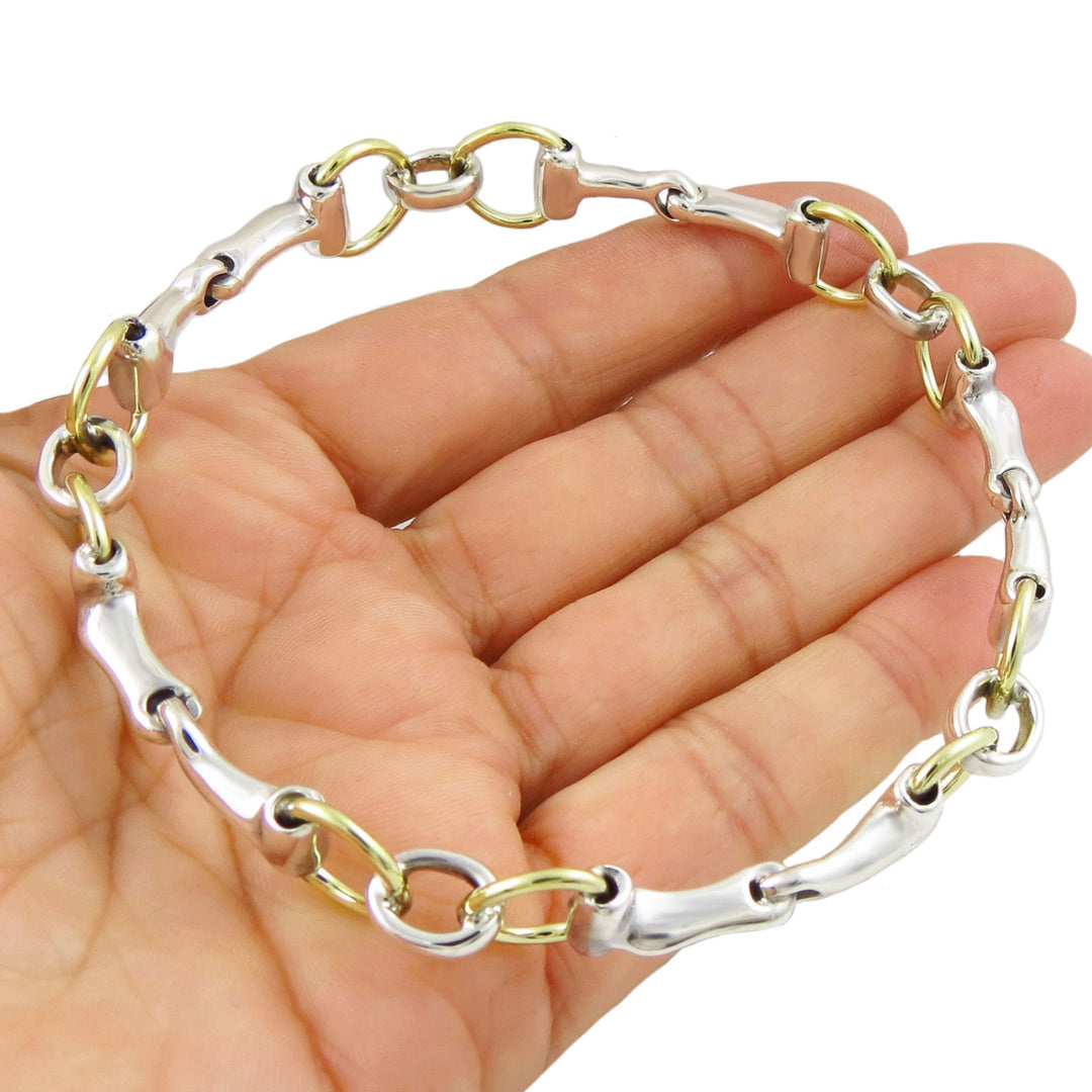 Mixed metal sterling 925 silver and gold horse snaffle bit equestrian riding tack bangle bracelet on a hand against a white background