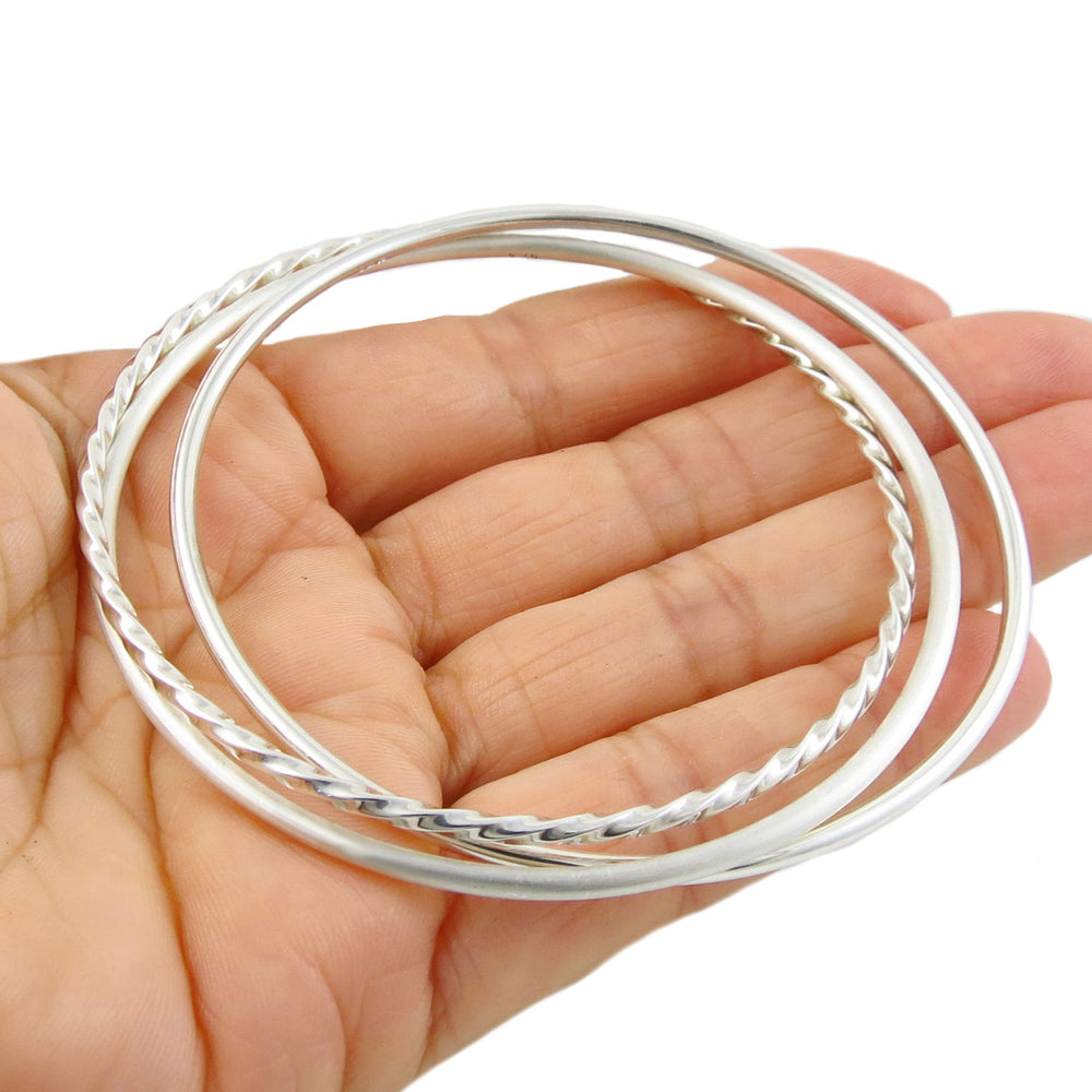 Three silver circle bangle stack held in a hand on a white background. 