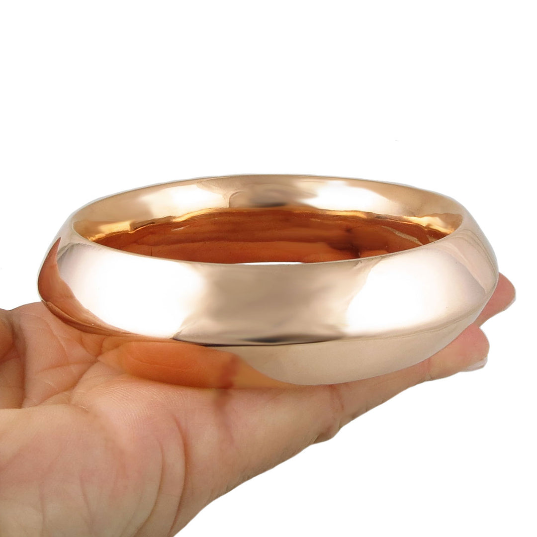 Large copper tube bangle held in a hand against a white background
