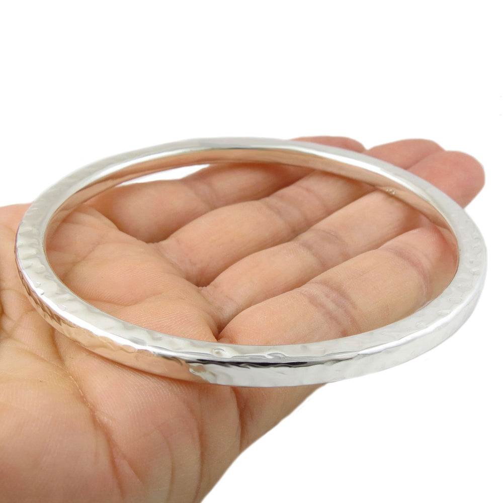 Hammered silver bangle on a hand against a white background