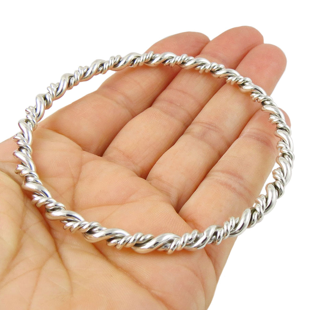 Coiled silver rope bangle on a hand against a white background