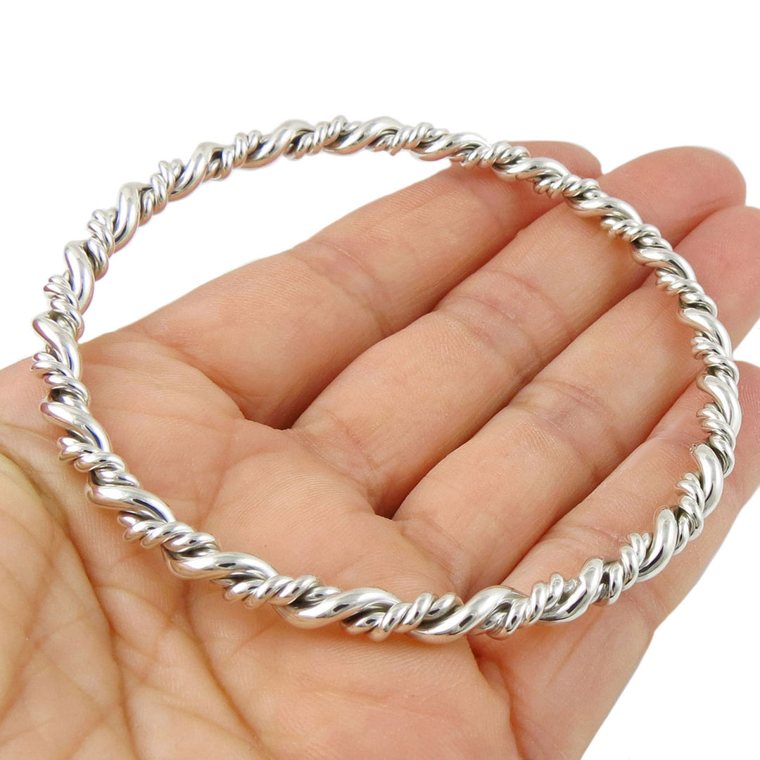 Silver rope bangle on a hand against a white background. 
