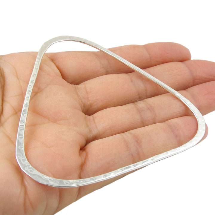A large sterling silver triangle bangle with a hammered finish held in a hand on a white background 