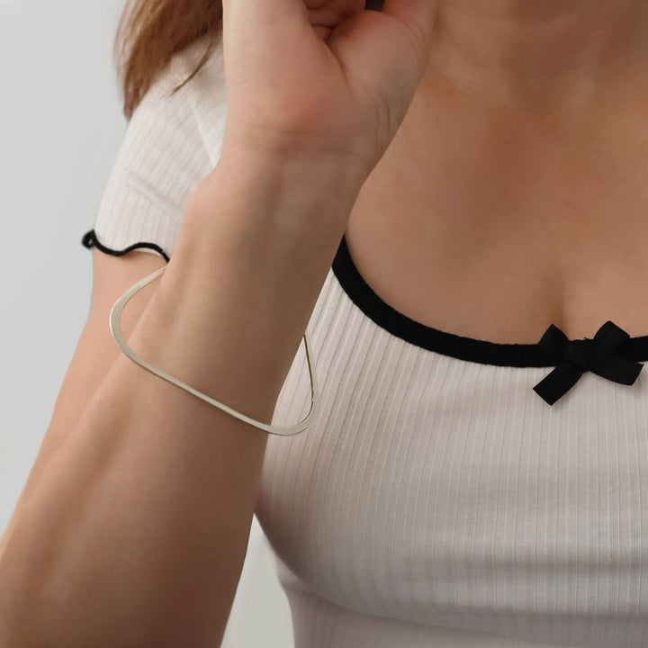 Close-up of a person wearing a white sleeveless top with black trim and a bow, wearing a large triangle shaped silver bangle.