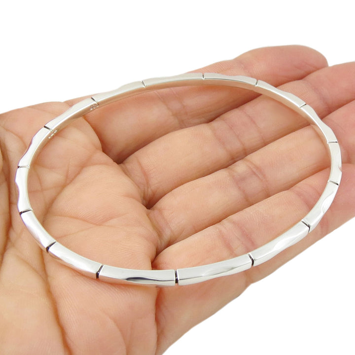 UK 925 sterling silver bangle featuring a symmetrical bamboo patternheld in a hand against a white background