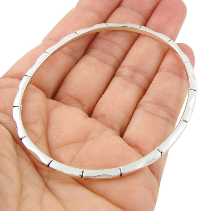 A large oval 925 sterling silver bangle with an unusua;l bamboo design held in a person's hand on a white background