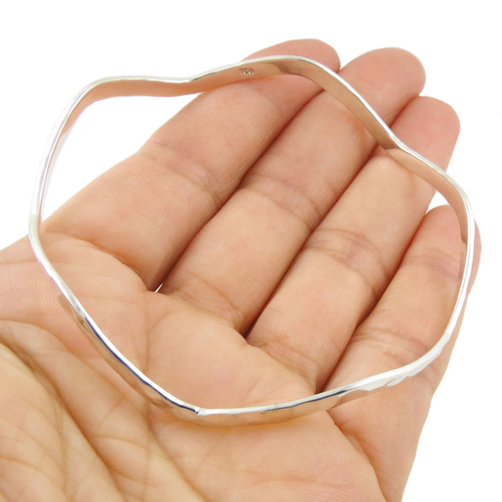 Sterling silver curved bangle held in a hand against a white background