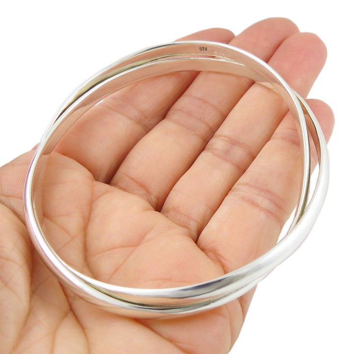 Hallmarked British Sterling silver double oval bangle held in a hand against a white background