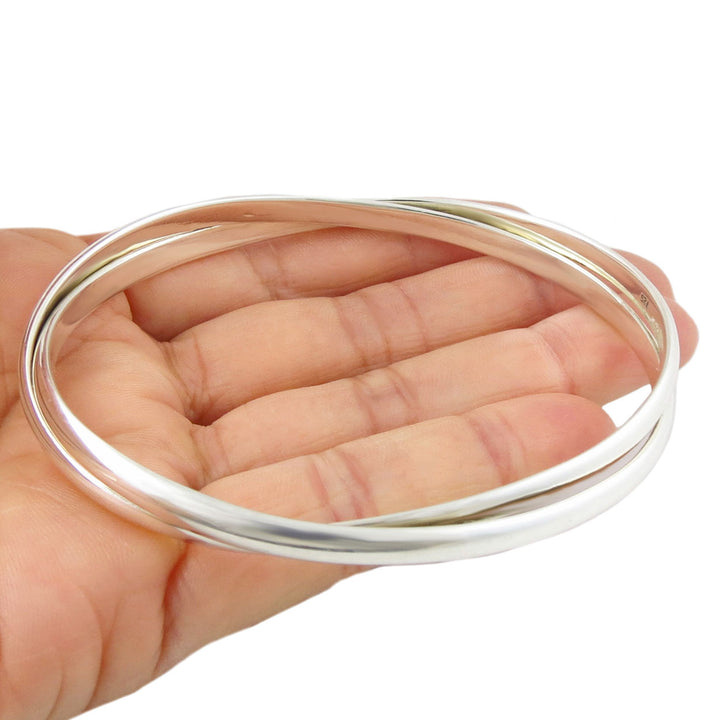 A large Mexican bangle in polished 925 sterling silver featuring two large interlocking oval bands held in a person's hand 