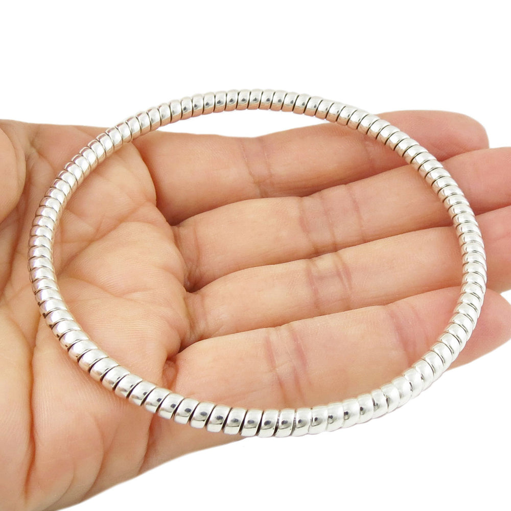 A large 925 sterling silver circle bangle with a twisted rope pattern held in a person's hand on a white background. 