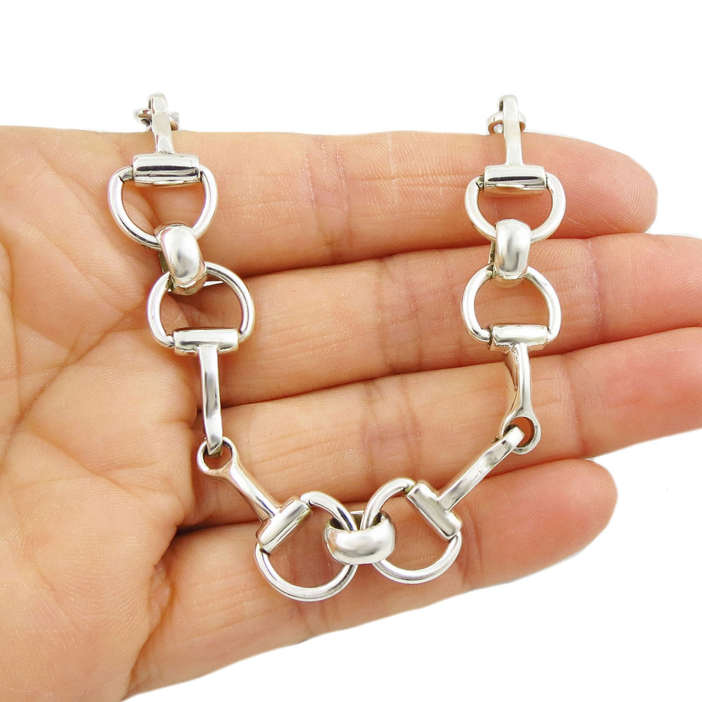 A sterling silver bracelet with snafflebit links being held in a hand on a white backround