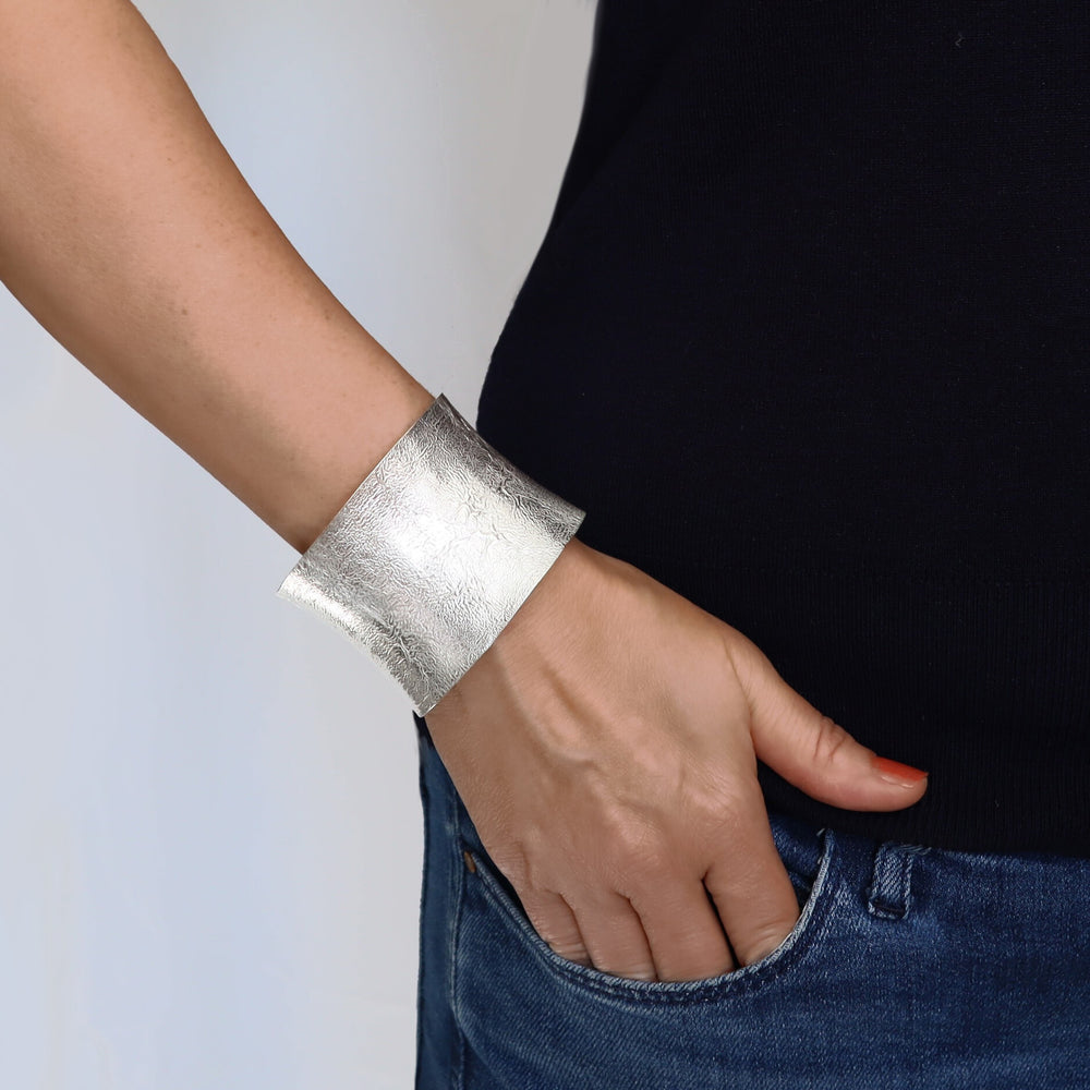 A woman wearing a wide textured reticulated sterling silver cuff bracelet.