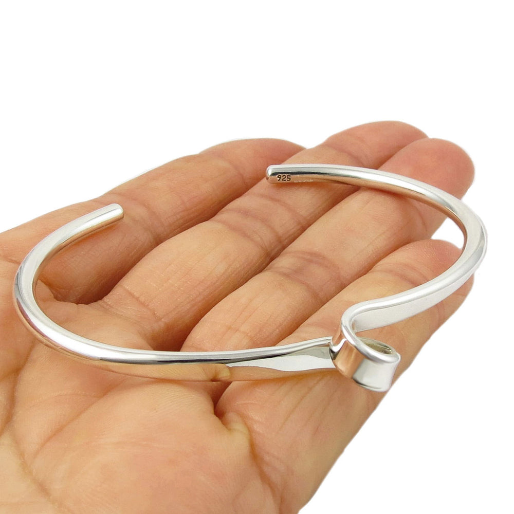 A large handmade Mexican sterling silver bracelet cuff with a large spiral detail at the front held in a person's hand on a white background
