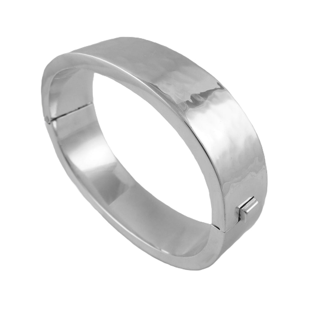A chunky silver oval bangle bracelet with a hand-hammered finish and a hidden hinge.