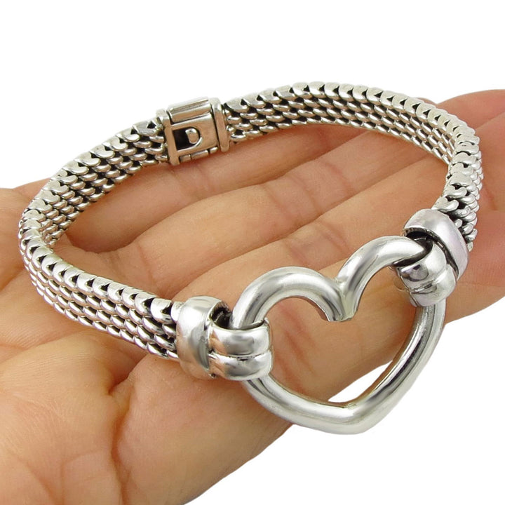 Silver bracelet with a large heart-shaped cnetre link held in a hand on a white background