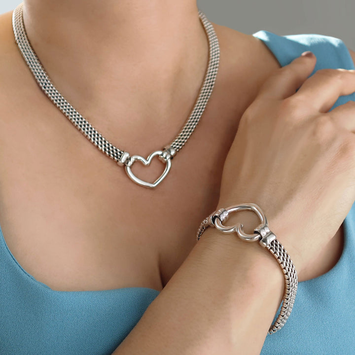 Silver necklace and matching bracelet with heart charm worn by a person against a blue background
