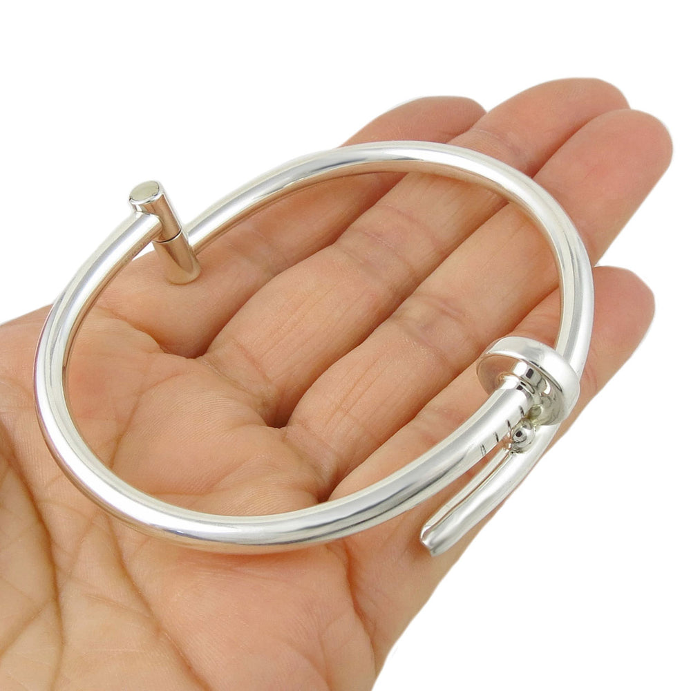 A large hinged 925 sterling silver nail bracelet cuff held in a woman's hand. 