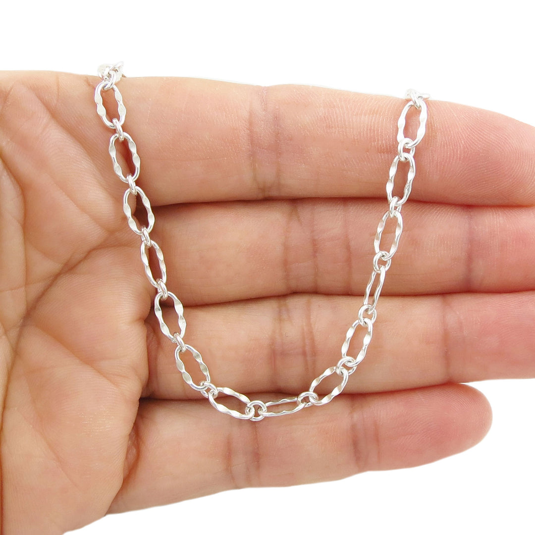 An oval link sterling silver chain bracelet with a hammered finish held in a persons hand. 