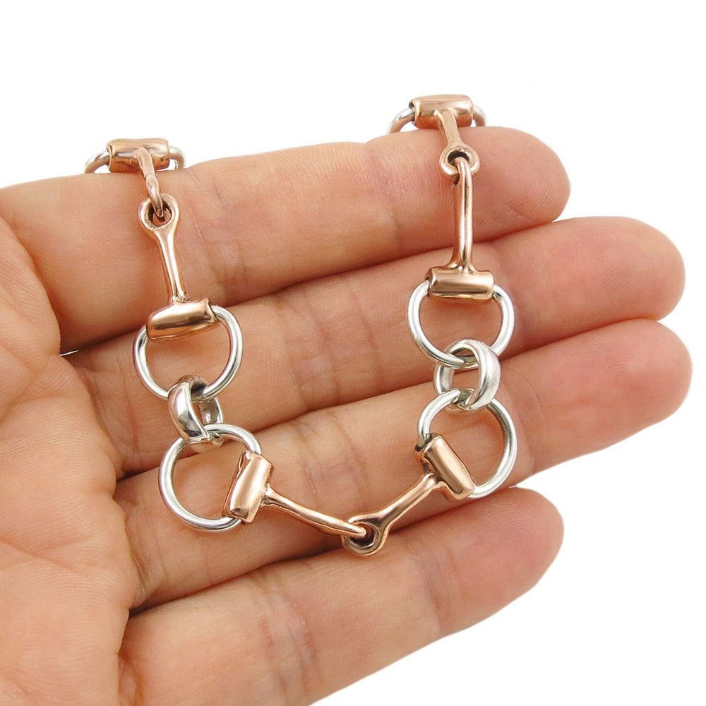 Copper and silver equestrian-themed horsebit bracelet on a hand against a white background