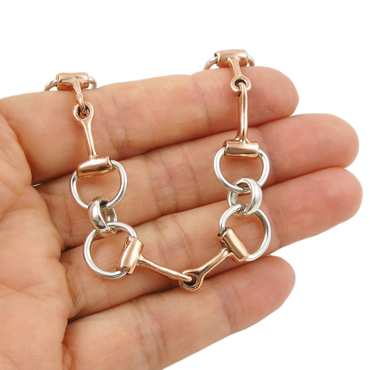Copper and silver equestrian-themed horsebit bracelet on a hand against a white background