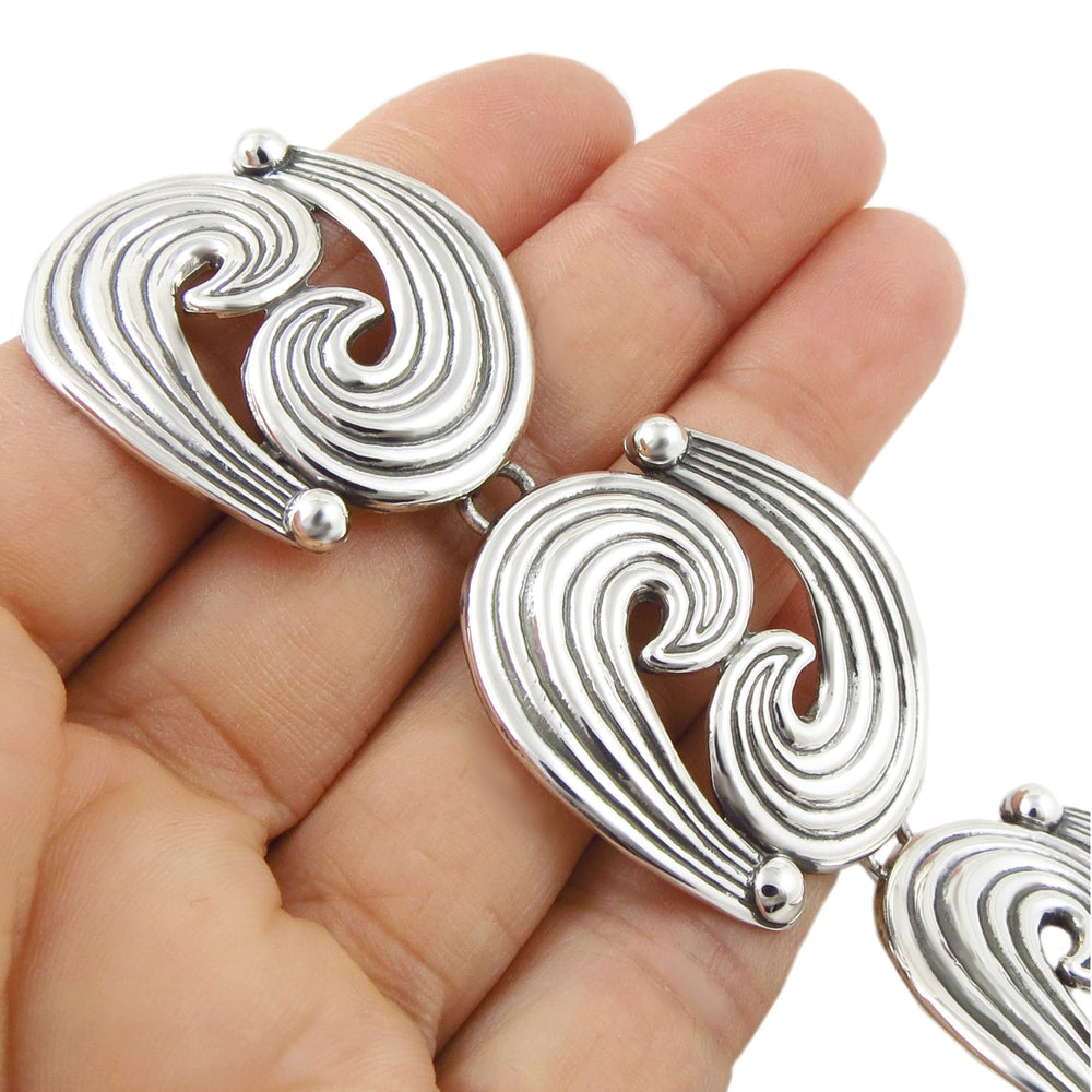 Silver bracelet with wave design links held in a hand against a white background