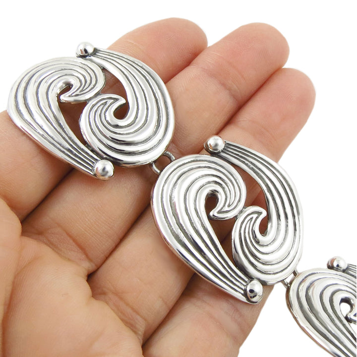 Silver bracelet with wave design links held in a hand against a white background