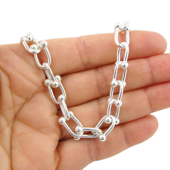 Silver gauge link chain bracelet held in a hand against a white background
