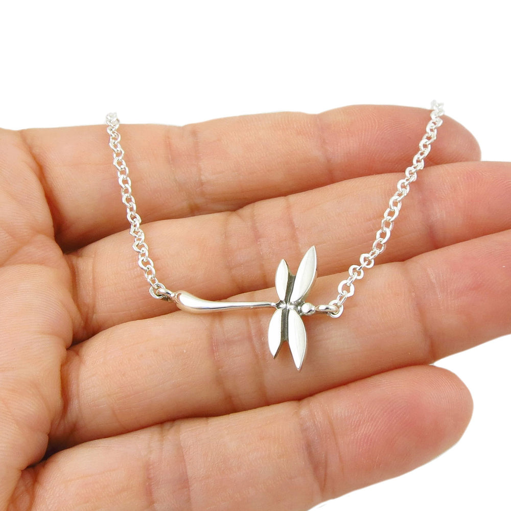 Silver bracelet with a delicate dragonfly link held in a hand against a white background