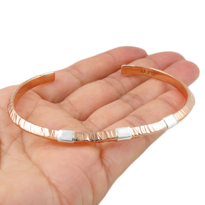 Copper and silver bracelet on a hand against a white background