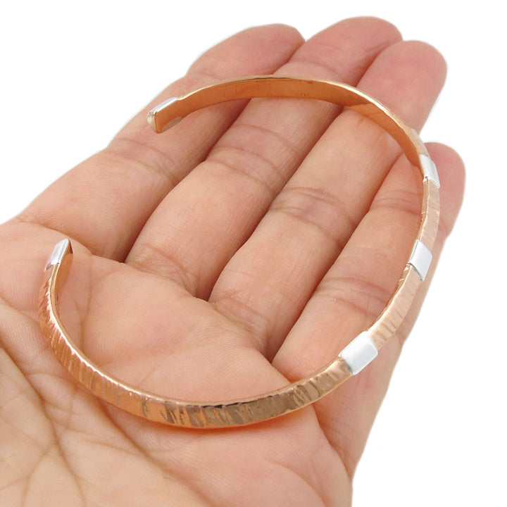 Copper bracelet with silver accents on a hand against a white background