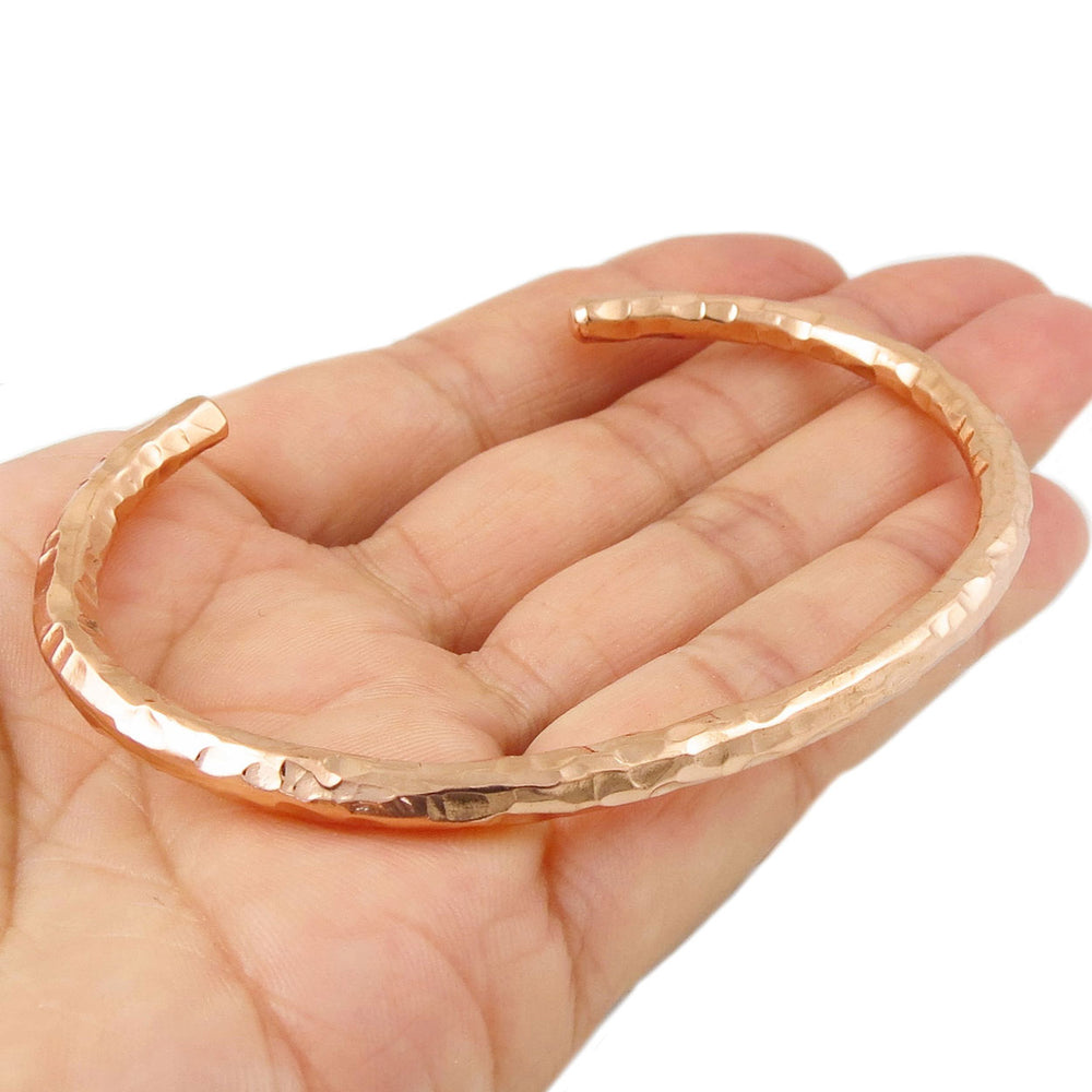 Solid hammered copper bracelet held in a hand on a white background