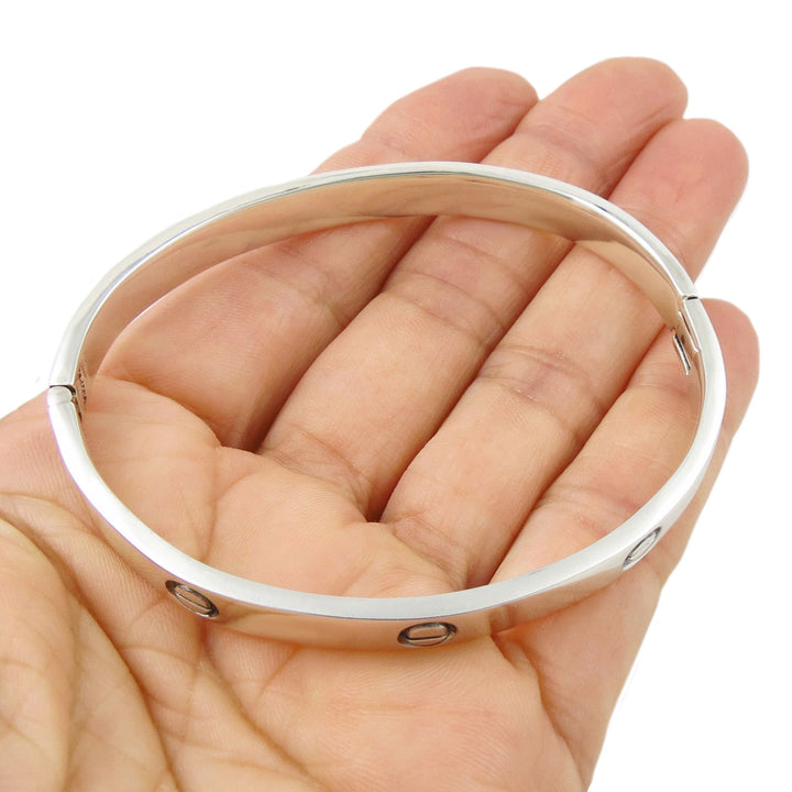 Silver bangle held in a hand against a white background