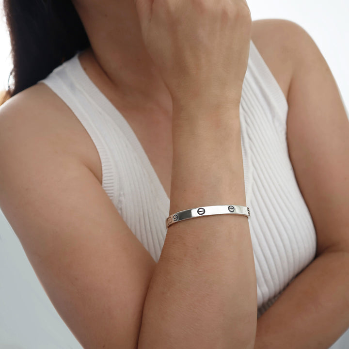 Woman wearing a silver bracelet with rivet screw accents on a plain background