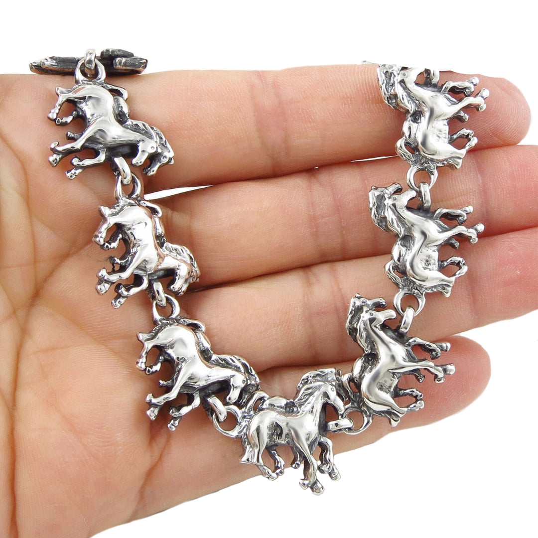 Silver bracelet with equestrian horse links held in a hand against a white background